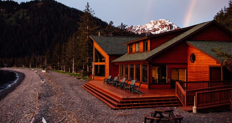A view of the Kenai Fjords Wilderness Lodge at sunset with a rainbow formed behind it