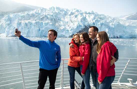 A group of people on Kenai Fjords Tours boat take a selfie on the deck.