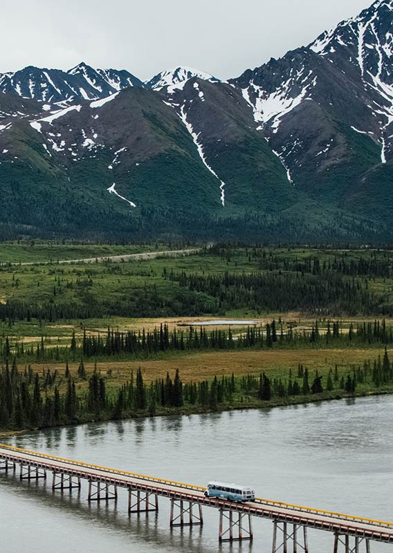 A tour bus crossed a large bridge over water with mountains in the background.