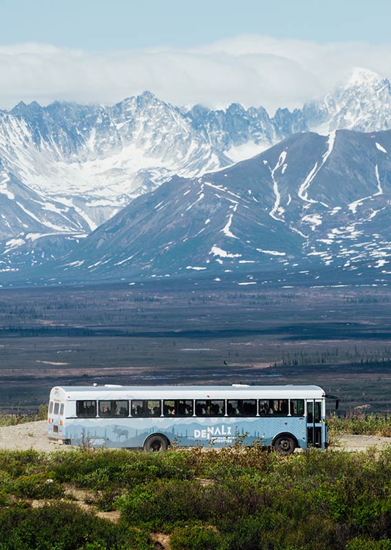 A bus is centered on a road with mountain range behind it.