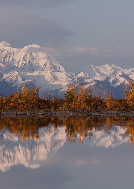 A view of snow covered mountains reflected in calm water.