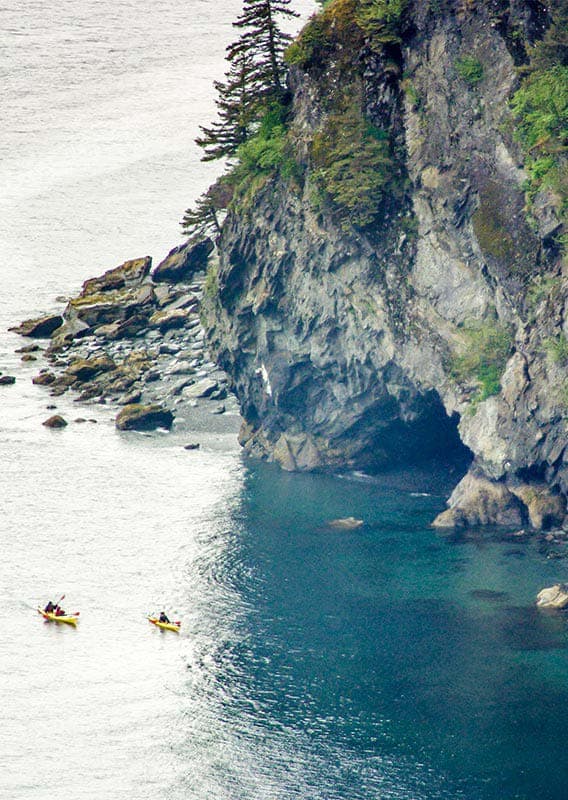 Kayakers on the sea next to rocky cliffs.