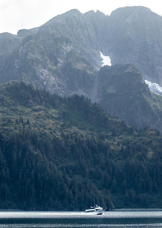 A boat cruises along the sea below forested mountainsides.