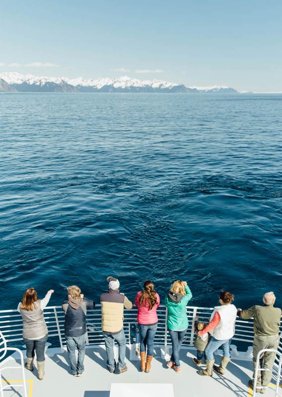 People stand at front of Kenai Fjords Tours boat on a sunny day