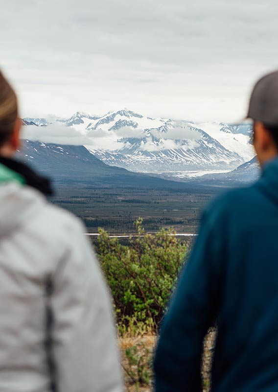 A couple look out past a cliff to a mountain range.