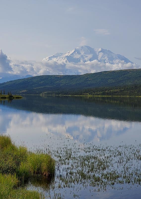 A view across a calm lake towards a tall snow-covered mountain in the distance.