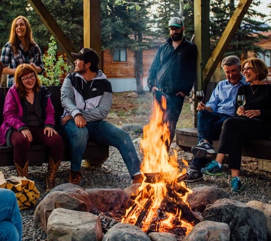 A group of people sit around a bonfire laughing and smiling
