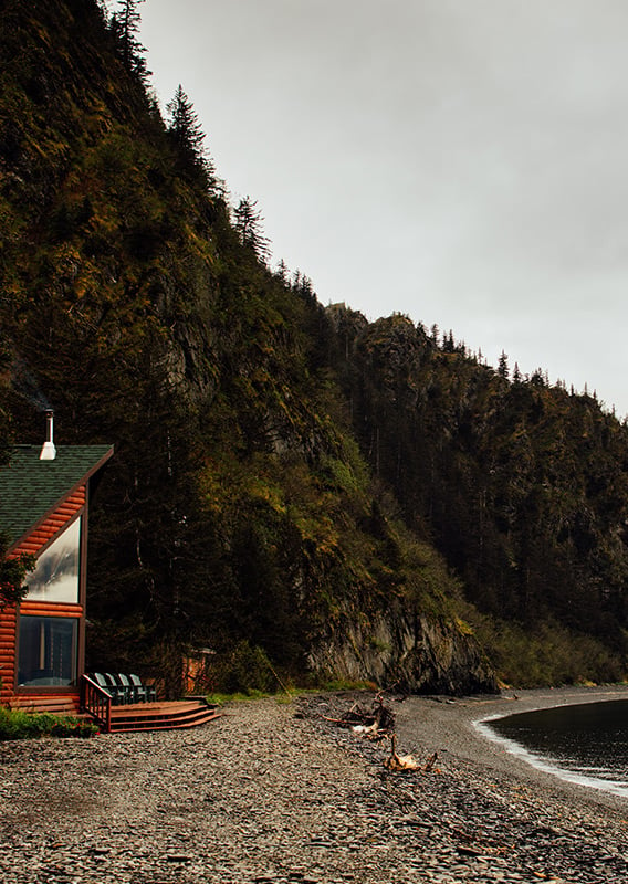 A wooden lodge with large windows overlooking the seashore.