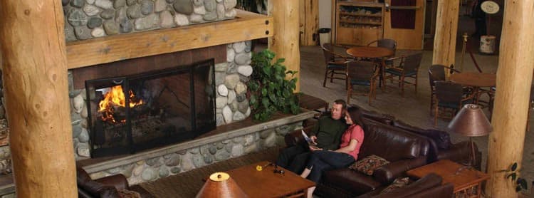 Two people sit in a hotel lounge next to a large fireplace.