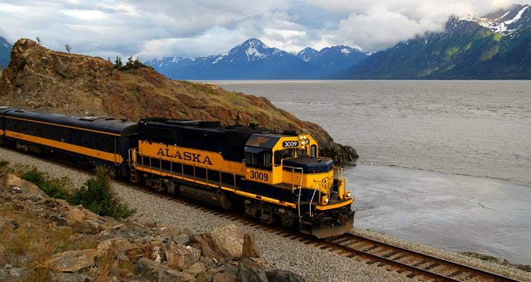 A train rides along the railroad alongside a lake.