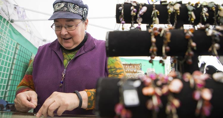 A woman puts jewelry together behind a display of her work