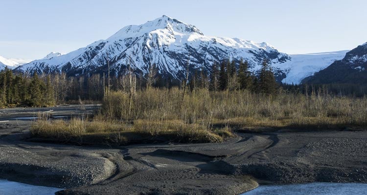 A snow-covered mountain rises above forested terrain and a