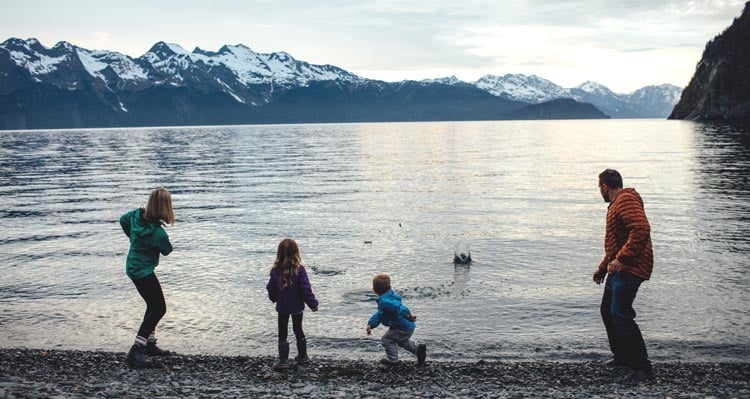 Family skipping stones over a lake, mountains behind.