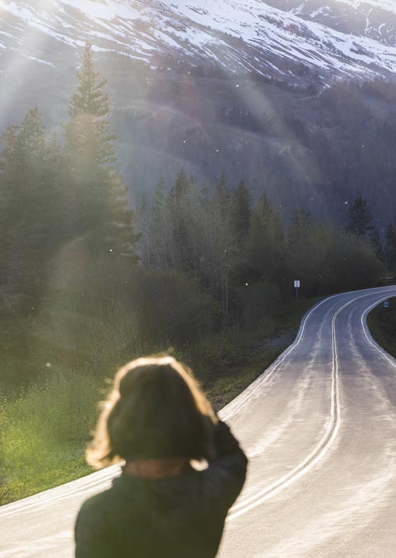 A person stands on a winding road alongside a rocky river 