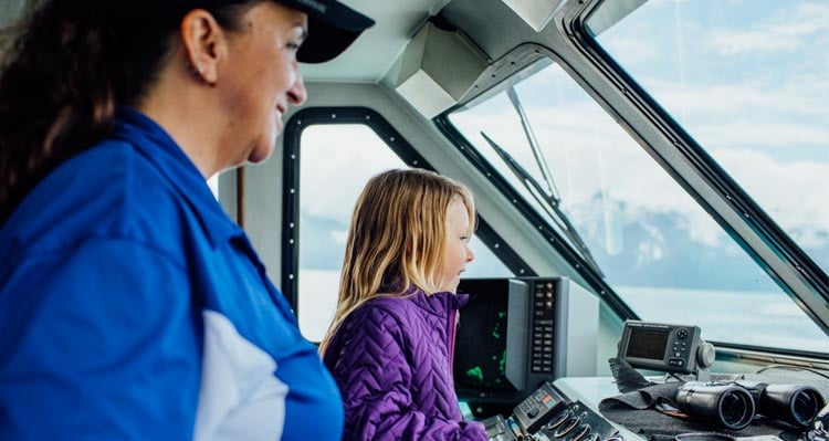 A child stands at a boat's helm with the captain