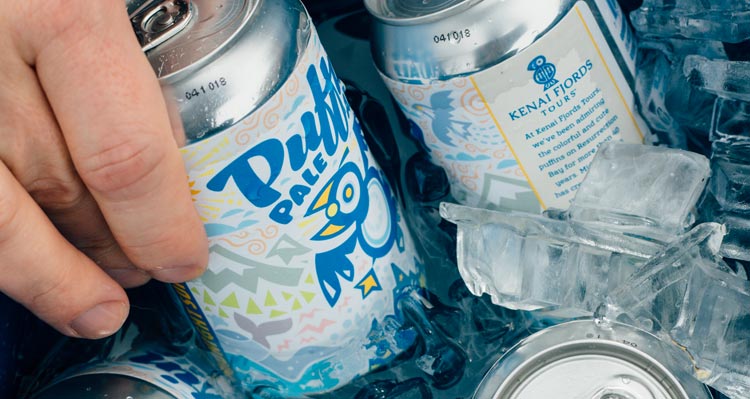 A hand reaches for a can of Puffin Pale Ale out of a cooler.