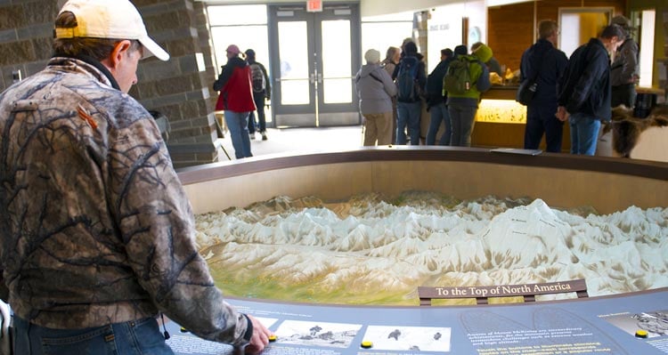 A person stands at a three-dimensional interpretive display of the Alaska Range.