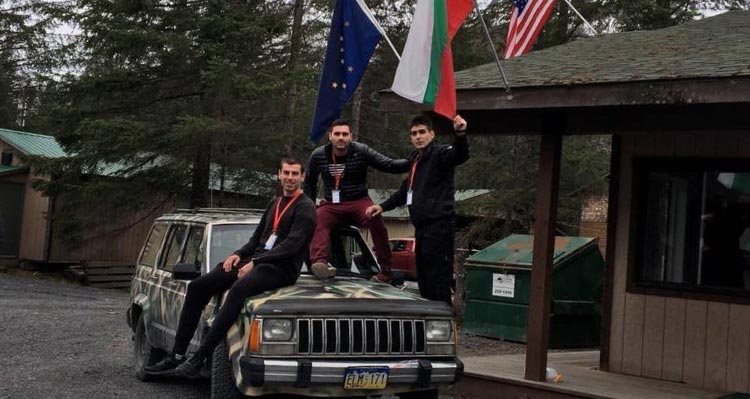 Three people sit on a car holding a Bulgarian flag.