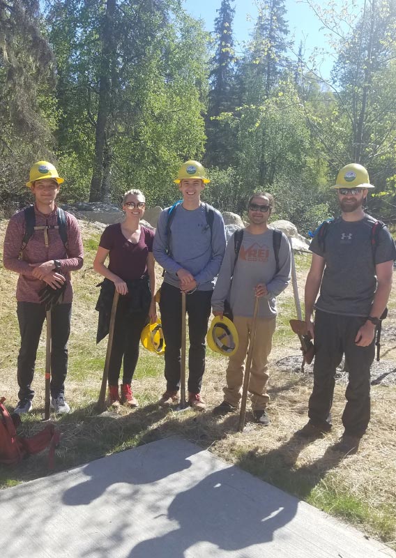 A group of people with hard hats and shovels get ready to work on trail building