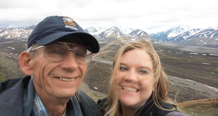 A close-up of two smiling people before an expansive tundra.