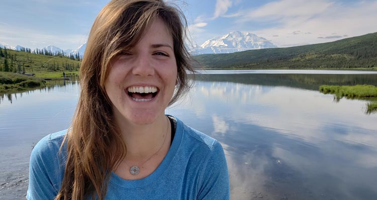A woman smiles in front of a lake and tundra terrain.