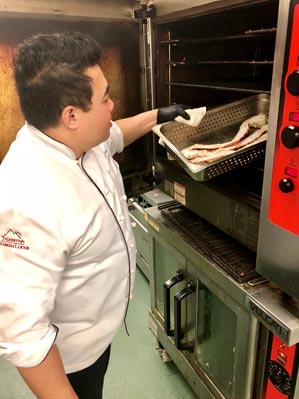 A chef takes Alaska King Crab legs out of an oven.