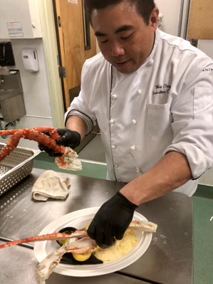 A chef places Alaska King Crab legs on a dinner plate.