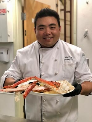 A chef holds a dinner plate of Alaska King Crab legs.