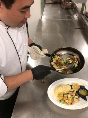 A chef plates vegetables on a plate.