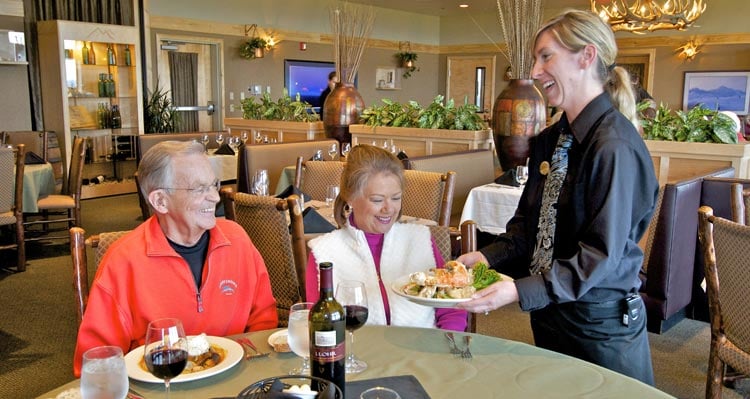 A server brings a plate of king crab to a couple seated for dinner.