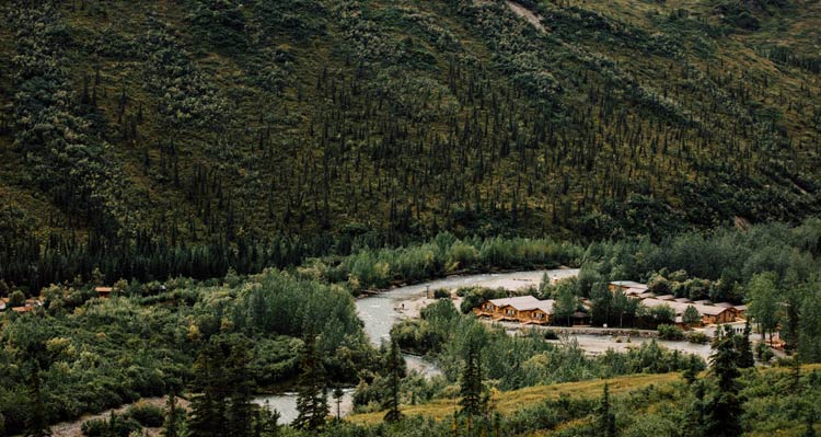 A series of wooden lodges nestled between forests and a rushing river