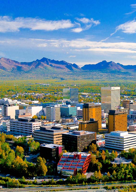 The skyline of Anchorage, Alaska sits before a mountainous landscape.
