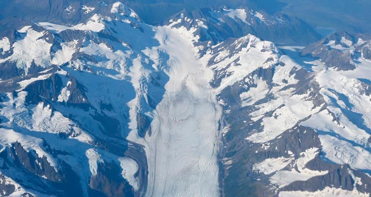 An aerial view of a glacier between ice-covered mountains.
