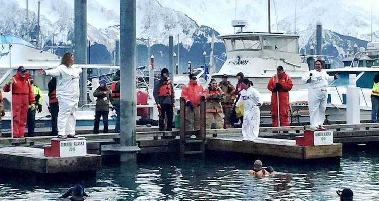 Many people stand on a dock. Two of them get ready to jump into ice-cold water.