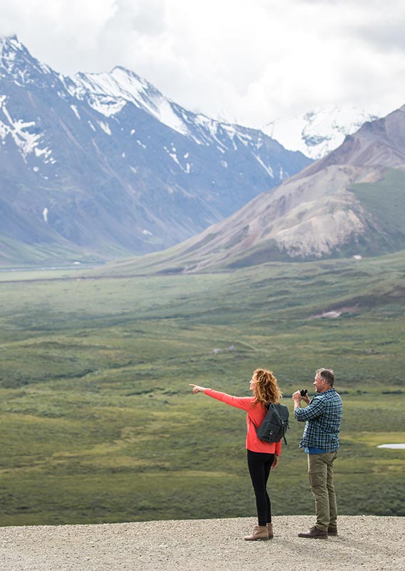 Two people overlook a a river and tundra landscape.