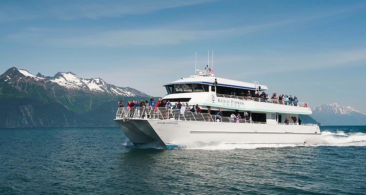 A boat cruises on a blue sea below mountains.