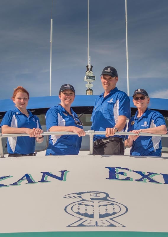 Four members of a boat crew stand at the stern of a white boat.