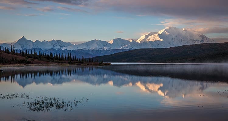 A mountain range in the distance behind a lake and forest.