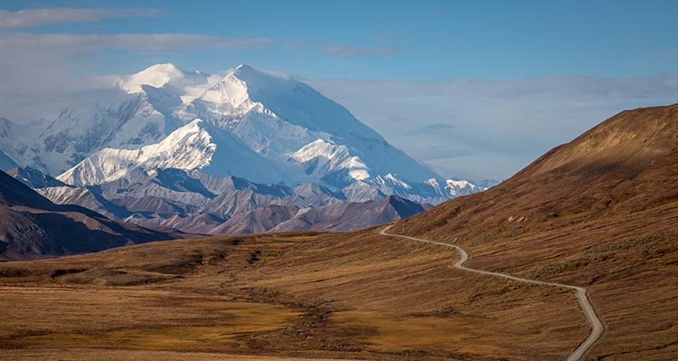 A road winds across orange tundra towards tall mountains.