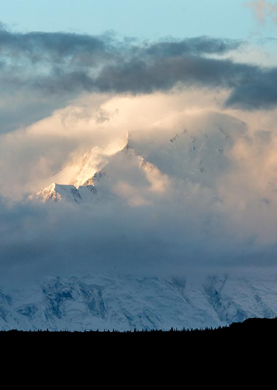 Denali, a tall snow-covered mountain between clouds.