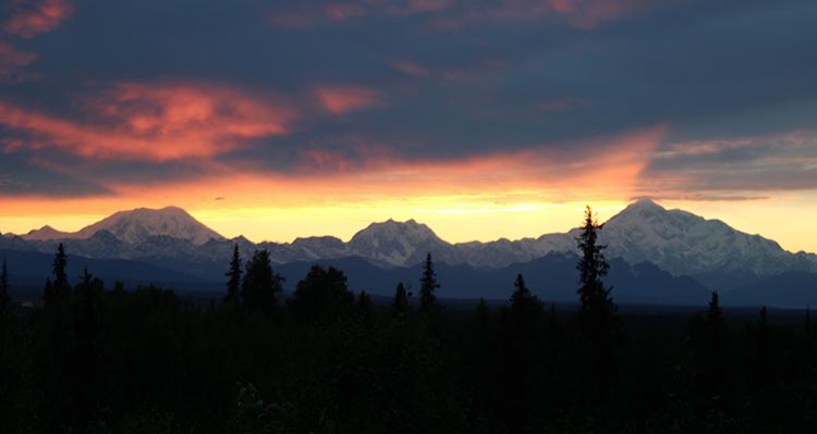 A view of the Alaska Range mountains under a red sky and sunset