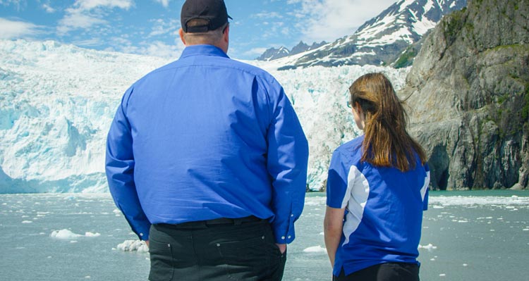 Two people look at a large glacier from a boat.