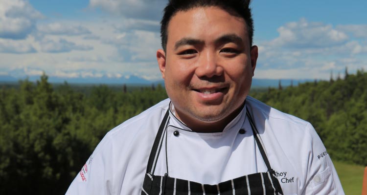 Chef Wes Choy standing in front of a wide forest and mountain vista.