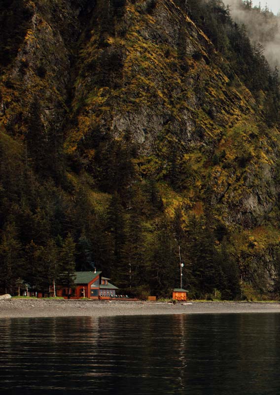 A view of the Kenai Fjords Wilderness Lodge below a green rocky cliffside.