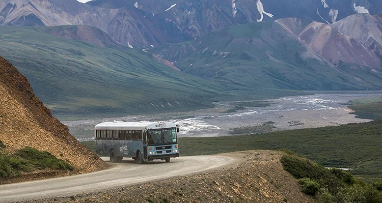 A bus rounds a corner along a mountainside road.