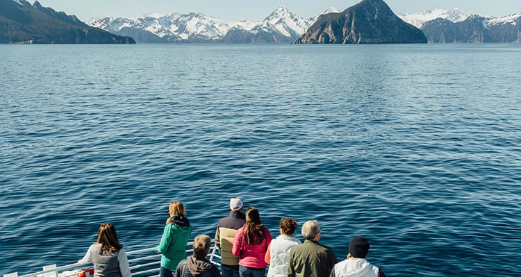 A group of people stand at the front of a boat looking towards mountain scenery.