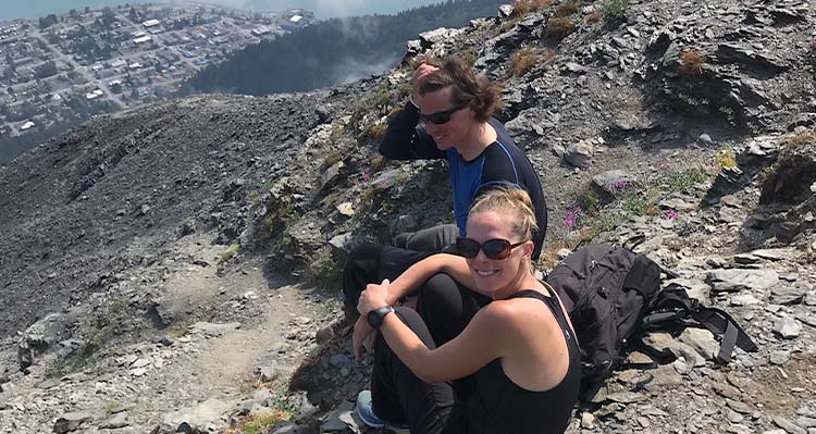 Two people sit at a rocky outcropping overlooking the town of Seward