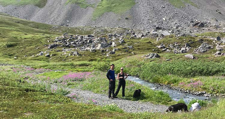 Two people stand next to a river through a meadow.