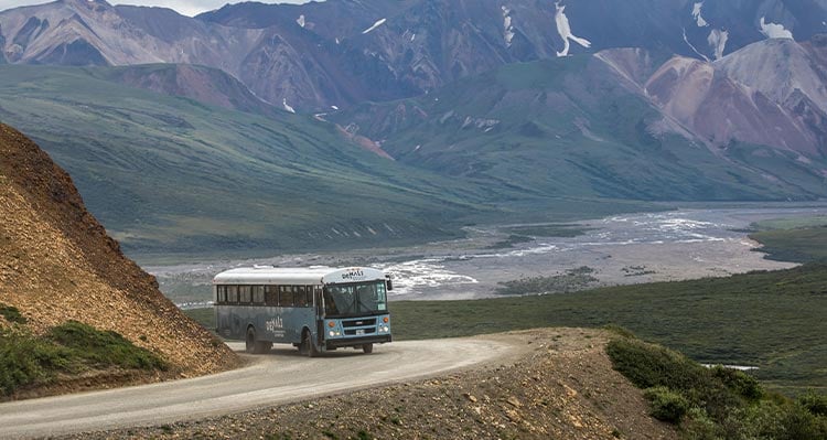 A blue bus rounds a corner along a mountainside.