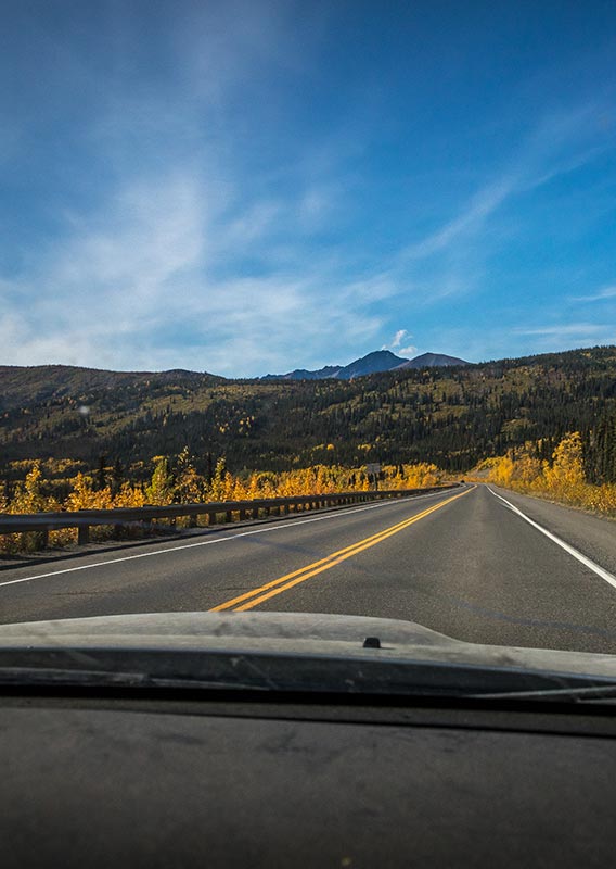 A view down a road towards tree-covered mountains.